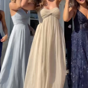 Champagnefärgad långklänning med twistad byst - Säljer en elegant champagnefärgad långklänning med twistad detalj över bysten och plisserad kjol. Klänningen är axelbandslös och har en luftig, flowy passform som ger en romantisk känsla. Från Nelly, finns inte kvar på hemsidan längre. Väldigt lång, jag är 167cm för referens. (Lånad första bild)