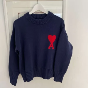 Mörkblå stickad tröja från Ami Paris - Mörkblå stickad tröja från Ami Paris med stor röd hjärtlogga på bröstet. Perfekt för en stilren och trendig look.