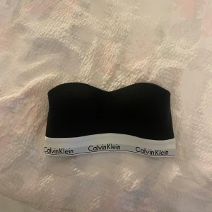 Svart tubtopp från Calvin Klein - Svart tubtopp från Calvin Klein med vit elastisk kant där loggan syns tydligt. Enkel och stilren design, perfekt för en avslappnad look. Den är helt oanvänd och axelband tillkommer🥰