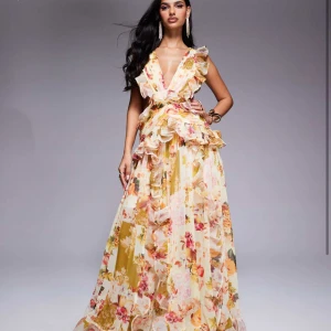 Blommig långklänning med volanger och öppen rygg - Säljer en slutsåld maxiklänning från ASOS som är helt ny med lappar kvar, nypris 1700kr.  Klänningen har djup v-ringning, volangdetaljer och en vacker öppen rygg. Perfekt för bal eller sommarens speciella tillfällen. Materialet är lätt och luftigt.