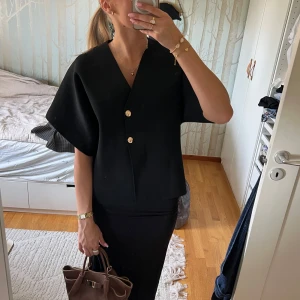 Svart topp med guldknappar - INTRESSEKOLL! Stilren svart toll med v-ringning och två dekorativa guldknappar. Den är i strl L men är mer oversized på mig som brukar ha Xs💞knappt använd, kontakta mig vid intresse!🥰