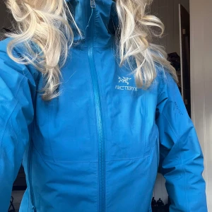 Blå skaljacka från Arc'teryx - Säljer en blå skaljacka från Arc'teryx (Zeta sl) i mycket fint skick med huva och dragkedja framtill. Jackan har två sidofickor med dragkedja och hög krage. Perfekt för utomhusaktiviteter och skyddar mot vind och regn. Jackan är 2 år gammal och mest hängt i en garderob så goretexen kan behövas fylla på. Strlk M kvinna.