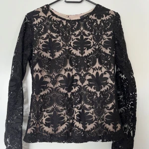 Blus/topp, Reserved, svart, L - Elegant svart spetsblus med långa ärmar från Reserved i storlek L (liten i storleken, vänlig se mått). Blusen har ett vackert blommönster och en rund halsringning. En stilig detalj är den triangulära öppningen på baksidan. Genomskinliga ärmar i övrigt är tröjan ej genomskinlig pga innertyg. Polyester, polyamide och elastan. Blusen är i nyskick.   Mått: Längd ca 60 cm Byst mätt från armhåla till armhåla ca 40 cm Midja ca 40 cm Ärmlängd mätt från axeln ca 63 ca Axel till axel ca 40 cm
