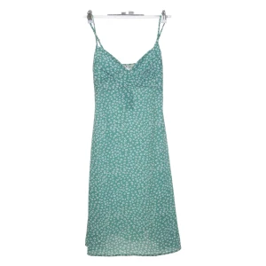 Grön blommig klänning  - Söt grön klänning med vita små blommor från Belle Vannes. Klänningen har smala axelband och v-ringad halsringning. Perfekt för varma dagar och har en lätt, luftig känsla. Sömmen har gått sönder vid v-ringningen men går lätt att fixa med något stygn eller säkerhetsnål 