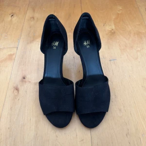 Svarta klackskor från H&M - Skor från H&M. Storlek 36. Använda en gång. Små märken (se bild) från att ha stött i marken finns men inget som syns mycket eller stör funktionen. Materialet är typ som mockaimitation. Klacken mätt från insidan är ca 5,5 cm, från utsidan ca 7,5 cm. Finns fler bilder!