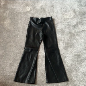 Svarta utsvängda byxor i skinnimitation från Zara - Säljer ett par svarta byxor i skinnimitation från Zara. Byxorna har utsvängda ben och hög midja, vilket ger en trendig siluett. Perfekta för dig som vill sticka ut med en cool look.