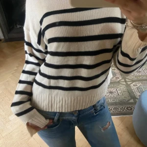 Vit och svart randig stickad tröja - Säljer en vit stickad tröja med svarta horisontella ränder. Tröjan har lång ärm, rund halsringning och ribbade muddar vid ärmslut och nederkant. Perfekt för en avslappnad och stilren look.