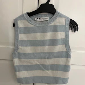 Randig stickad linnetopp från Zara - Säljer en stickad linnetopp från Zara i ljusblått och vitt med breda horisontella ränder. Toppen är ärmlös och har en rund halsringning. Perfekt för varmare dagar och enkel att matcha med jeans eller kjol.
