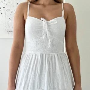 Hollister Vit sommarklänning  - Superfin vit lång klänning med smala axelband, knyt framtill och smockad rygg från Hollister. Aldrig använd! Lätt och luftig med volanger och diskret prickigt mönster.Perfekt för varma dagar och midsommar💗I storlek small