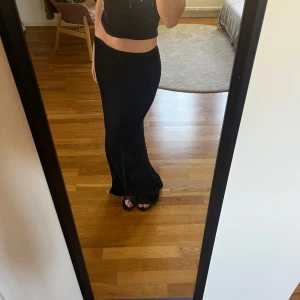 Svart långkjol med slits - Säljer en svart långkjol med slits framtill. Kjolen har en figurnära passform och är enkel i designen, vilket gör den lätt att styla. Perfekt för dig som gillar stilrena plagg med en twist.