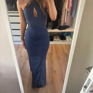 Marinblå långklänning med halterneck och cut-out - Säljer en marinblå långklänning med halterneck och snygg cut-out detalj framtill. Använd endast en gång så i väldigt bra skick! Klänningen har en tight passform och är ärmlös, perfekt för bal eller fest. Materialet är slätt och stretchigt för en smickrande siluett. Storlek 32/4!