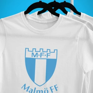 Vit Malmö FF t-shirt - Vit t-shirt med stort blått Malmö FF-tryck på bröstet. Klassisk rund halsringning och korta ärmar. Perfekt för dig som vill visa ditt stöd för laget på ett stilrent sätt.