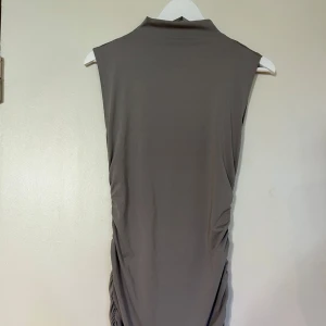Grå ärmlös klänning - SHEIN  - Snygg grå ärmlös klänning med hög krage och rynkade detaljer på sidorna. Perfekt för en stilren look.