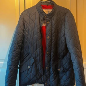 Blå quiltad jacka från French Laundry - Säljer en snygg blå quiltad jacka från French Laundry. Jackan har en stilren design med knappar framtill och två fickor. Insidan är röd vilket ger en fin kontrast. Perfekt för kyligare dagar! Storlek L. 