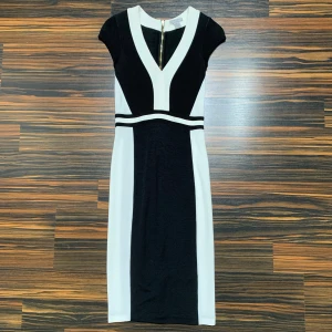 Svart och vit klänning från H&M - Snygg svart och vit klänning från H&M med en elegant v-ringning och dragkedja i ryggen. Klänningen har en figurnära passform och korta ärmar, perfekt för en stilren look.