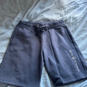 Mörkblåa shorts från Sail Racing - Snygga mörkblåa shorts från Sail Racing med snörning i midjan och tryckt logga på benet. Perfekta för en avslappnad stil.