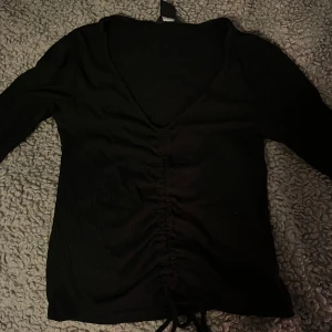 Svart ribbad topp med snörning - Snygg svart ribbad topp med v-ringning och snörning framtill. Perfekt för en stilren look.