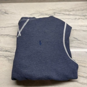 Blå hoodie från Polo Ralph Lauren - Säljer en snygg blå hoodie från Polo Ralph Lauren med kontrasterande vita sömmar. Den har en liten broderad logga på bröstet. Perfekt för en avslappnad stil. Skriv så fort ni har en fråga inte frågor är duma!!!