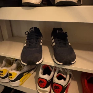 Adidas sneakers i mörkblått - Snygga Adidas sneakers i mörkblått med vita ränder och detaljer. Skorna har en klassisk design med snörning och en bekväm sula. Perfekta för en avslappnad stil.