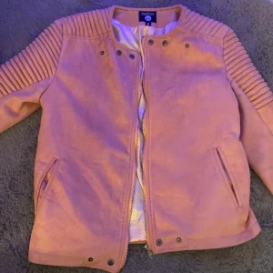 Rosa jacka från Boohoo - Säljer en snygg rosa jacka från Boohoo med ribbade detaljer på axlarna. Jackan har dragkedja och knappar framtill samt två fickor. Perfekt för en stilren look.