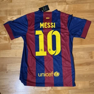 Blåröd fotbollströja från Nike - Säljer en blåröd randig fotbollströja från Nike med Messi och nummer 10 på ryggen. Tröjan har korta ärmar och klubbmärket på bröstet. Perfekt för fans av FC Barcelona.