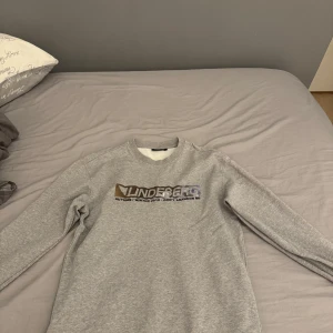 Grå tröja från J.Lindeberg - Säljer en stilren grå tröja från J.Lindeberg med texten 'AUTUMN / WINTER 2019 - DON'T ABANDON ME' tryckt på framsidan. Tröjan har långa ärmar och en rund halsringning. 