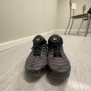 Svarta Nike sneakers med mönster - Säljer ett par svarta Nike sneakers med ett unikt rutigt mönster och vit swoosh-logga. Skorna har snörning och en rund tå, perfekt för en sportig look.