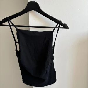 Svart topp - Snygg svart topp med smala axelband och en elegant design. Perfekt för en stilren look. Öppen rygg nyskick aldrig använd från Gina 