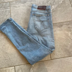 Tiger of sweden jeans - Säljer ett par ljusblå jeans med klassisk femficksdesign och en brun läderdetalj vid midjan. Jeansen har en slim passform och är perfekta för en avslappnad stil. Dom är 30/32. Är lagade men är inget som syns. Kom gärna med frågor.