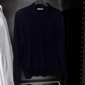 Svart merinoull pikétröja från Invento - Säljer en stilren svart pikétröja från Invento, tillverkad i 100% merinoull. Tröjan har långa ärmar och en klassisk krage med knappar. Kontakta för fler bilder eller eventuella funderingar. Har varit använt ett tag men inga defekter eller tecken på användning förutom en lagning i armhålan som inte syns, skriv för bild. Pris kan diskuteras vid snabb affär