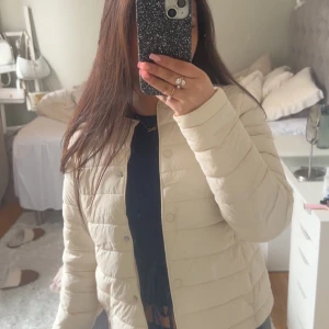 Beige quiltad jacka - Säljer en stilren beige quiltad jacka med dragkedja och knappar. Jackan har en normal passform och är perfekt för vår och höst. Den är långärmad och har en enkel design som passar till många olika outfits.