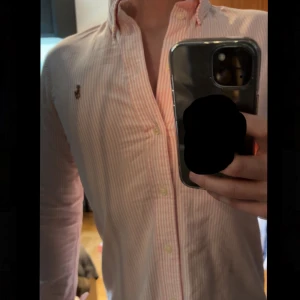 Ralph Lauren skjorta - Säljer en stilren rosa och vit randig skjorta från Ralph Lauren perfekt till sommaren. Skick är som ny inga fläckar,hål eller missfärgningar. Nypris 1800