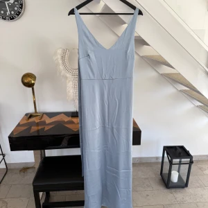 Ljusblå långklänning från Maya Deluxe - Säljer en elegant ljusblå långklänning från Maya Deluxe. Klänningen har en v-ringad design och smala axelband. Perfekt för speciella tillfällen med sin stilrena look.