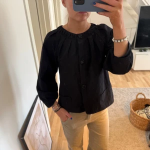 Svart kavaj, jacka  - Säljer en stilren svart kavaj jacka, blus med knappar framtill. Kavajen har en rundad hals och trekvartsärmar, vilket ger en elegant look. Perfekt för att komplettera din garderob med en tidlös klassiker.