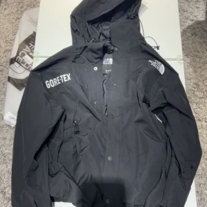 Svart Gore-Tex jacka från The North Face - Säljer en helt ny svart Gore-Tex jacka från The North Face. Jackan har en justerbar huva och dragkedja framtill. Perfekt för regniga dagar med sin vattentäta design. Logotypen är tryckt på bröstet och ärmen.