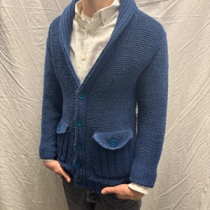 Humör kofta blå S - Säljer en snygg blå stickad kofta från Humör med knappar och två fickor framtill. Koftan har en ribbad krage och muddar. Plagget har storleken XS men sitter som S. Plagget är i bra skick men lite nopprig. Modellen är 182cm/67kg