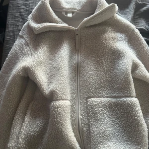  teddyjacka (Hm)  - Mysig beige teddyjacka med dragkedja framtill och hög krage. Perfekt för kyliga dagar med sina långa ärmar och mjuka material. Jackan har praktiska fickor på sidorna. Jackan är från hm och är i storlek XS