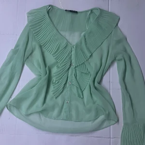 Fin turkose grön blus - Fin blus turkos grön långarmad med volanger runt handleden, halsen, nacken och lite ner med knappar som glimrar, blusen är i storlek S ifrån Zara och färgen är lite mer synlig i verkligheten än på bilderna men min kamera är inte så bra.