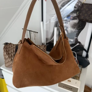 Brun väska HM - Snygg brun axelväska i mjuk mocka imitation från H&M. Ett långt band tillkommer. Inga tecken på användning, endast lite synligt vid dragkedjan. Se sista bilden.