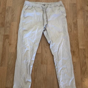 Beiga chinos med snörning från ASOS - Snygga beiga chinos från ASOS DESIGN med elastisk midja och snörning. Byxorna har raka ben, sidofickor fram och fickor bak. Tillverkade i mjuk bomull för extra komfort.