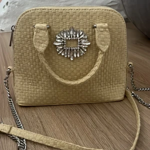 Beige handväska med strass från Zara - Snygg beige handväska från Zara i flätad look med glittrig strassdetalj framtill. Väskan har både handtag och axelrem i kedja, perfekt för att lyfta din outfit. Dragkedja upptill och stilren, boxig form.