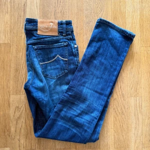 Jacob Cohën blå jeans med knappar - Snygga blå jeans från Jacob Cohën med klassisk femficksdesign, kontrastsömmar och knäppning med flera silverfärgade knappar. Jeansen har en läderpatch bak och är tillverkade i mjukt denimtyg som sitter skönt hela dagen.