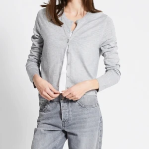 Ljusgrå kofta från 157 med knappar - Ljusgrå kofta från 157 med rund halsringning och knäppning framtill. Tröjan är i mjuk bomullsmix, har långa ärmar och ribbade muddar vid hals och ärmslut. Tröjan är använd 2-3 gånger och är i bra skick! 