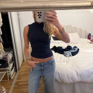 Mörkblå ärmlös polotopp - Säljer en mörkblå ärmlös polotopp med tight passform. Toppen har hög hals och är figurnära, perfekt att styla med jeans eller kjol. Enkel och stilren design utan mönster eller detaljer, tillverkad i mjukt stretchigt material.