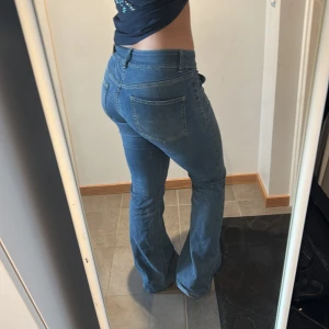 Blå bootcut jeans med fickdetaljer - Snygga blå jeans från Nelly med bootcut passform och låg midja. Jeansen har markerade sömmar längs benen och coola fickor framtill. Klassisk fyrficksmodell i mjukt denimtyg, perfekta för en avslappnad och trendig look.