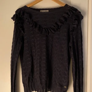 Mörkblå stickad tröja Odd Molly volang - Supersnygg mörkblå stickad tröja från Odd Molly med volangdetaljer längs ringningen. Tröjan har ett genombrutet mönster och långa ärmar. Perfekt för dig som gillar unika detaljer och en feminin touch. Ops! Tröjan har några stygn fram på tröjan som gått upp som syns på sida 4💐 syns dock inte från håll!🥂