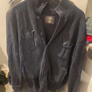 Mörkblå kofta från L.O.G.G. H&M - Snygg mörkblå kofta från L.O.G.G. H&M i storlek L. Koftan har ribbad krage, knäppning framtill med stora knappar och två bröstfickor med lock och knapp. Perfekt för lager-på-lager och chill stil.