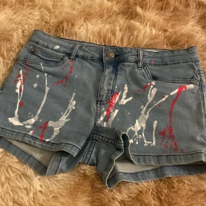 Pepperts jeansshorts med färgstänk - Snygga ljusblå jeansshorts från Pepperts i super skinny fit med coola röda och vita färgstänk framtill och baktill. Klassisk femficksmodell med knapp och dragkedja. Perfekta för dig som vill sticka ut med en kreativ och trendig look.