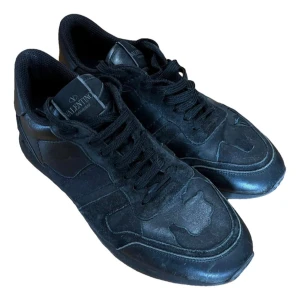 Svarta Valentino Garavani sneakers - Snygga helsvarta sneakers från Valentino Garavani med klassisk design. Skorna har ovandel i skinn och mocka, rund tå och svarta snören. Perfekta för dig som gillar stilrena och exklusiva sneakers med en lyxig känsla.