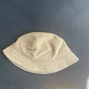 Beige bucket hat lager 157 - Stilren beige bucket hat från Kangol med klassisk form och diskret logga på insidan. Tillverkad i bomull, perfekt för soliga dagar och enkel att matcha med olika outfits. Mjuk och bekväm passform som ger en avslappnad vibe.